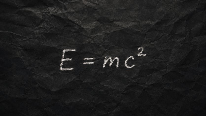 Albert Einstein's formula E=mc² written in white chalk on a black crumpled paper background.