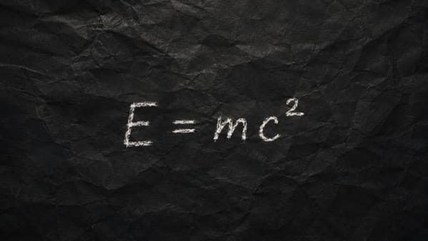 Albert Einstein's formula E=mc² written in white chalk on a black crumpled paper background.