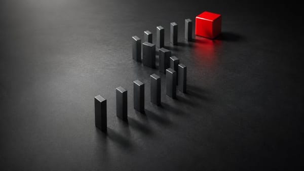 A line of black rectangular dominoes forming an S-shape curve stands on a dark, textured surface, leading towards a single red cube at the far end.